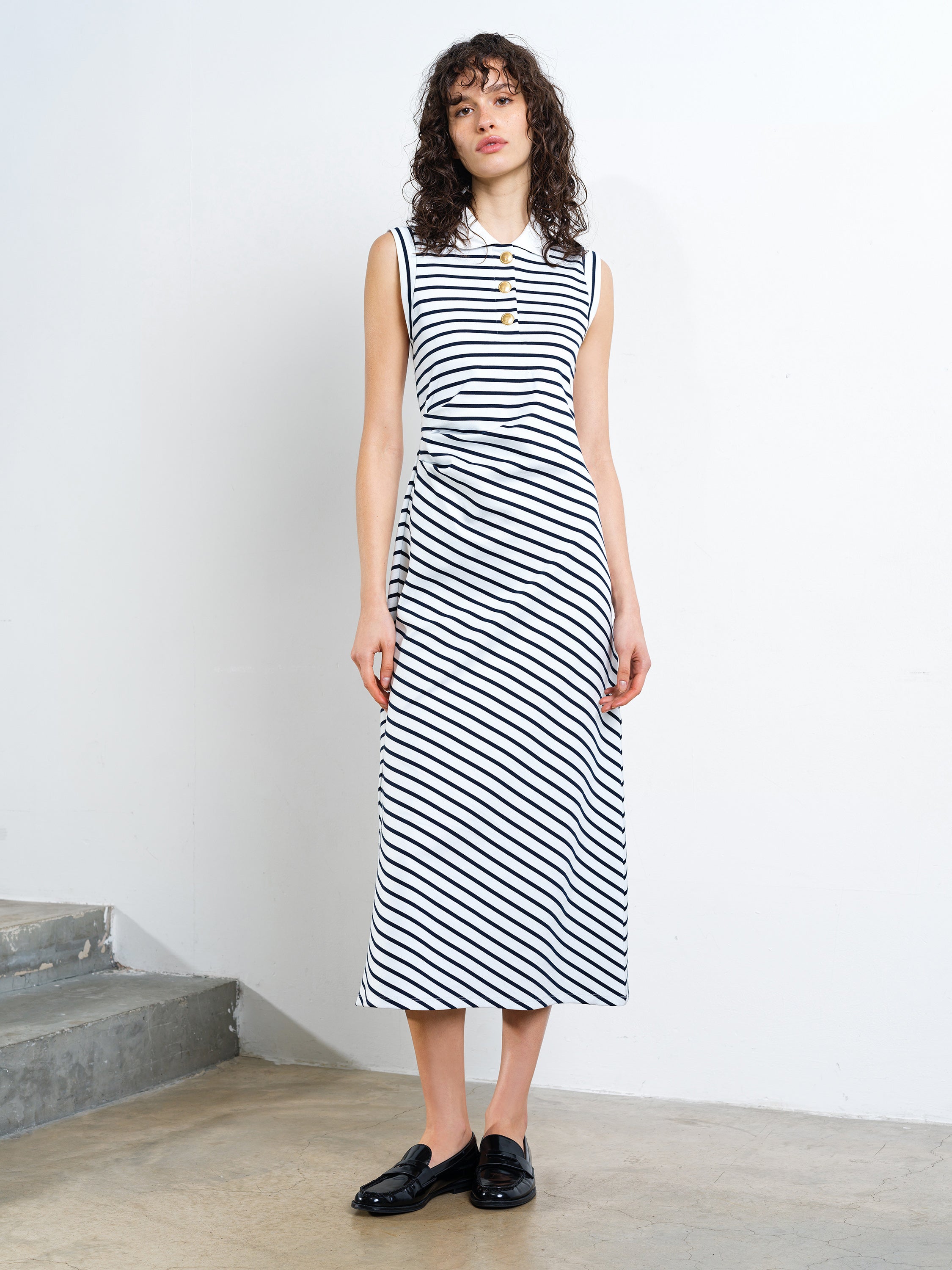 Woman wearing a black and white striped midi polo dress with gold button detailing
