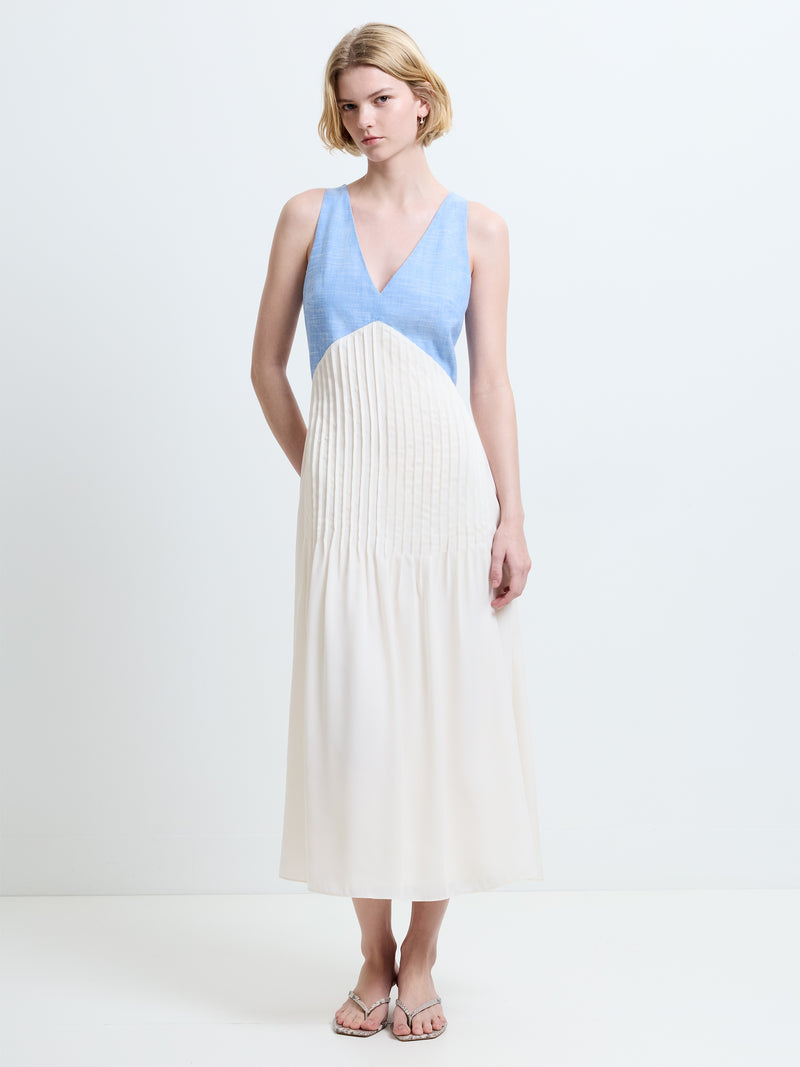 Woman wearing a sleeveless, V neck midi dress, with a chambray blue bodice and a contrasting cream skirt