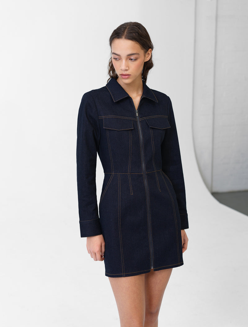Woman wearing a navy blue denim mini dress with long sleeves and contrast stitch detailing