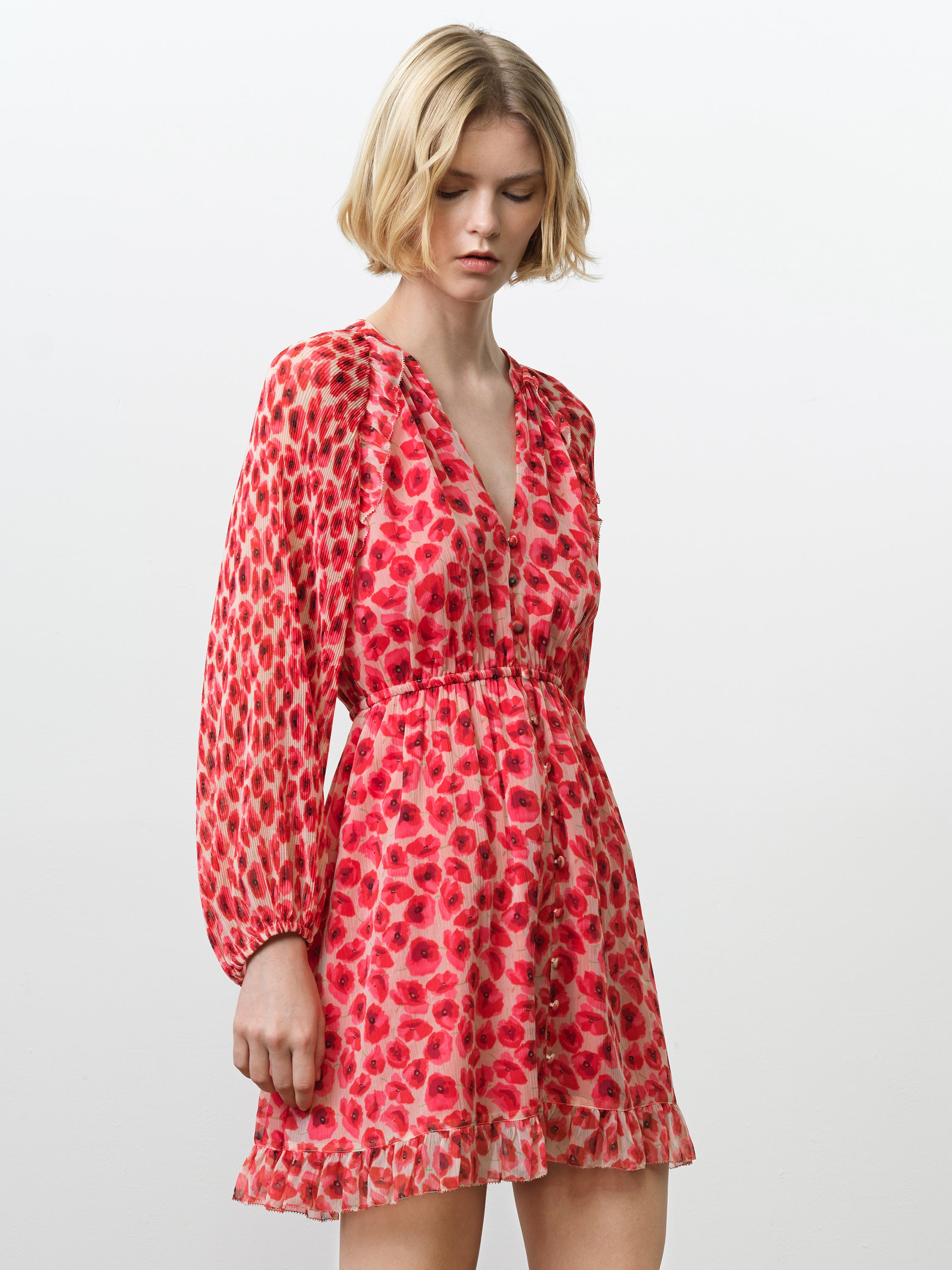 Woman wearing a long sleeve chiffon mini dress with a V neckline and a gathered waist in a bright poppy floral print