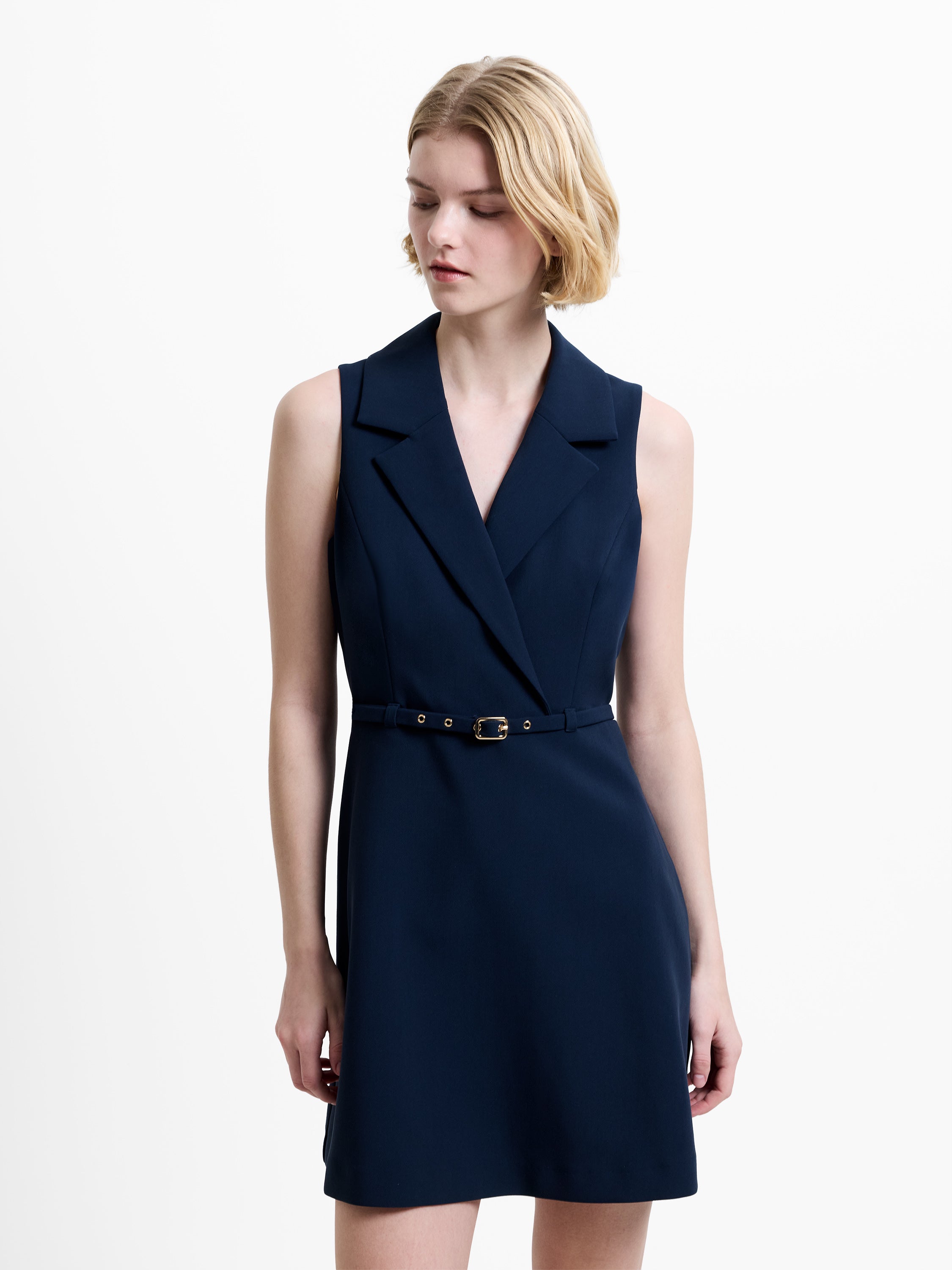 Woman wearing a sleeveless, navy mini dress with a lapel collar and a belted waist
