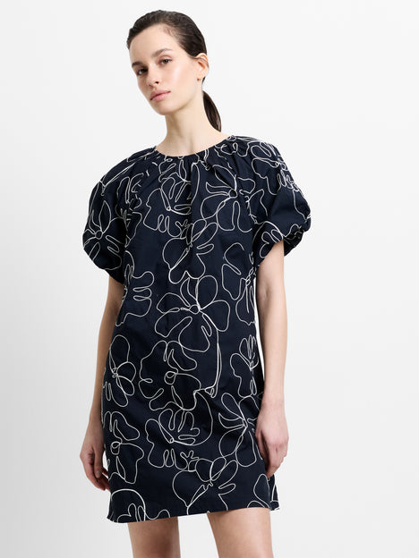 Woman wearing a black and white floral embroidered mini dress, with short puff sleeves and a round neckline
