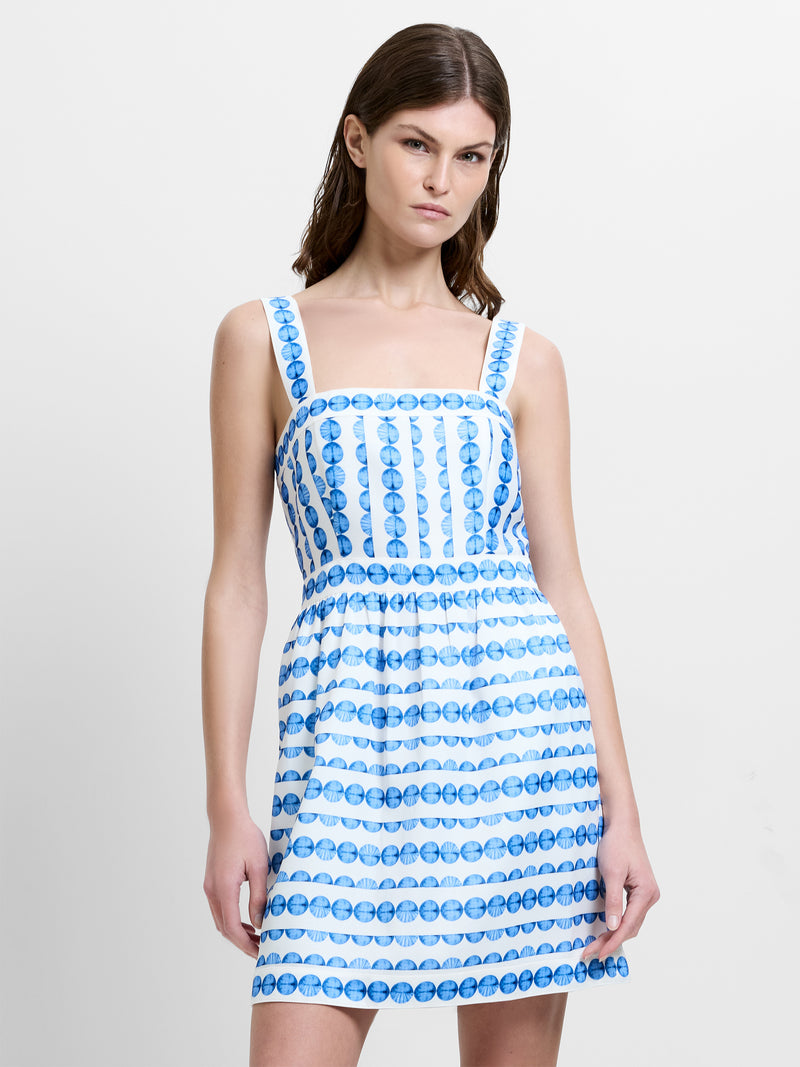 Woman wearing a blue and white patterned mini dress with straps and a square neckline