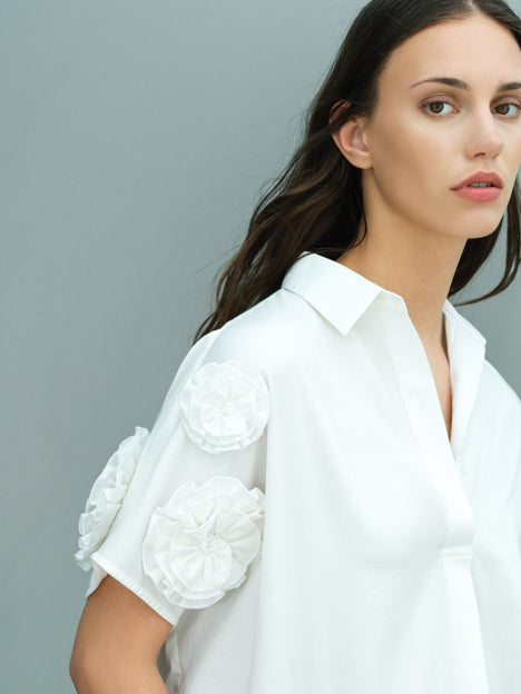 A woman wearing a cotton 3D floral short sleeved white popover over sized shirt with an open collar and relaxed fit.