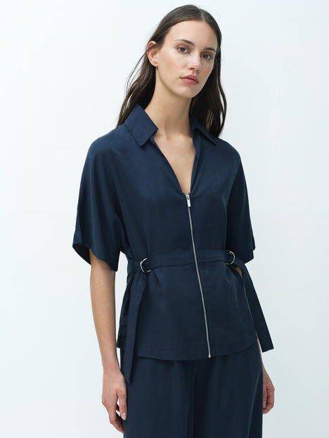 A woman wearing a relaxed fit navy blue shirt with a zip, D ring waist belt, open neckline and short sleeves.
