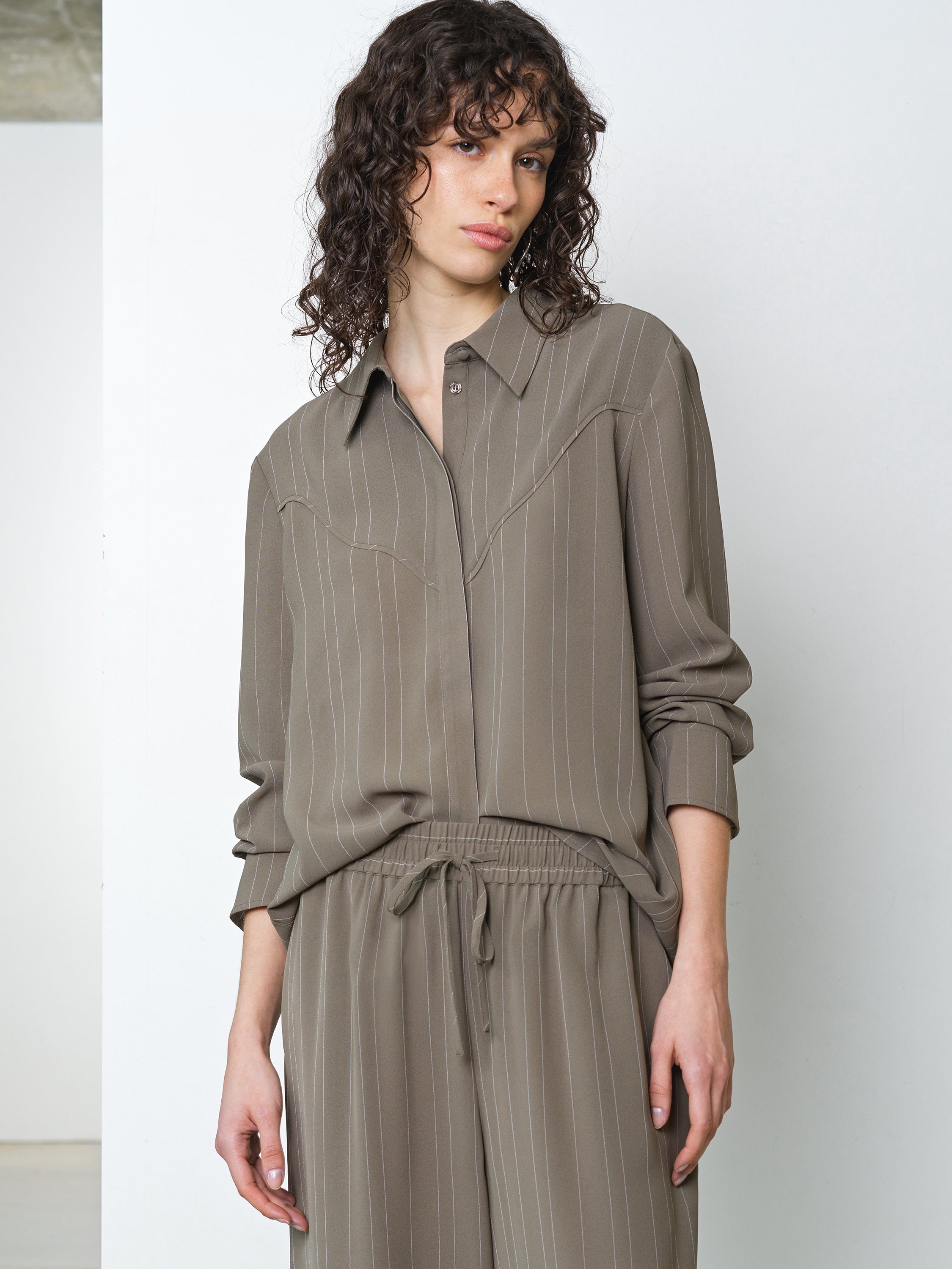 Woman wearing a long sleeve khaki pinstripe shirt with matching trousers