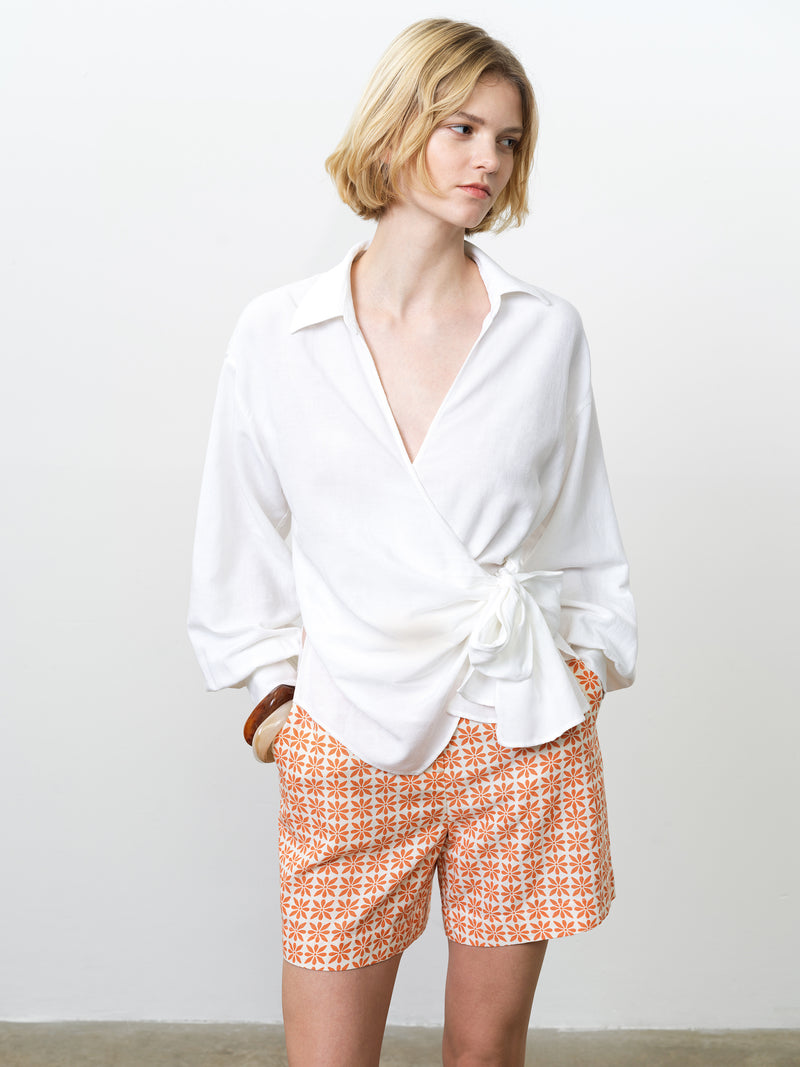 Woman wearing a white, wrap over linen shirt, with long dropped sleeves and a V neckline
