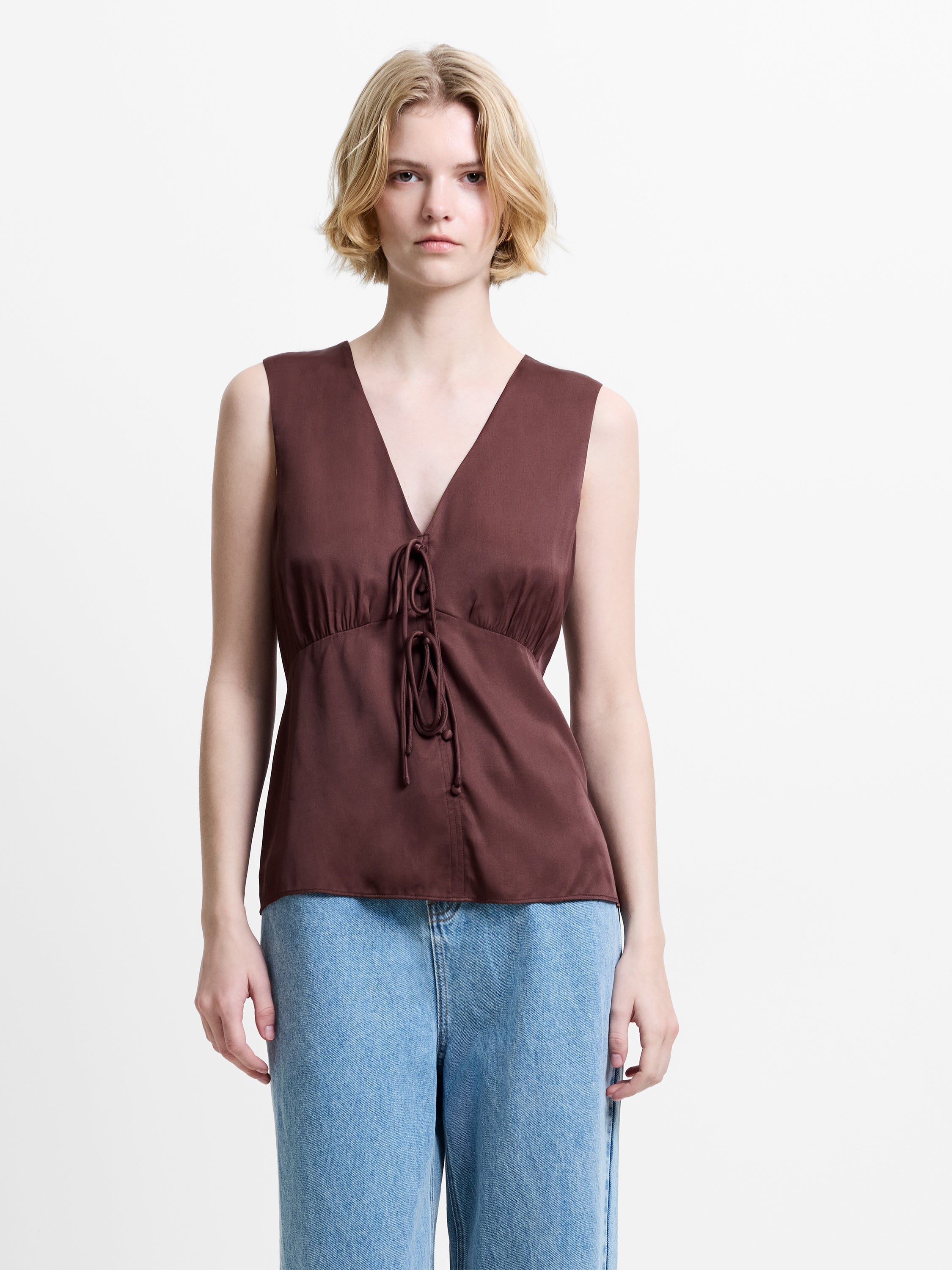 Woman wearing a brown satin sleeveless tank top with a V neckline and front tie details