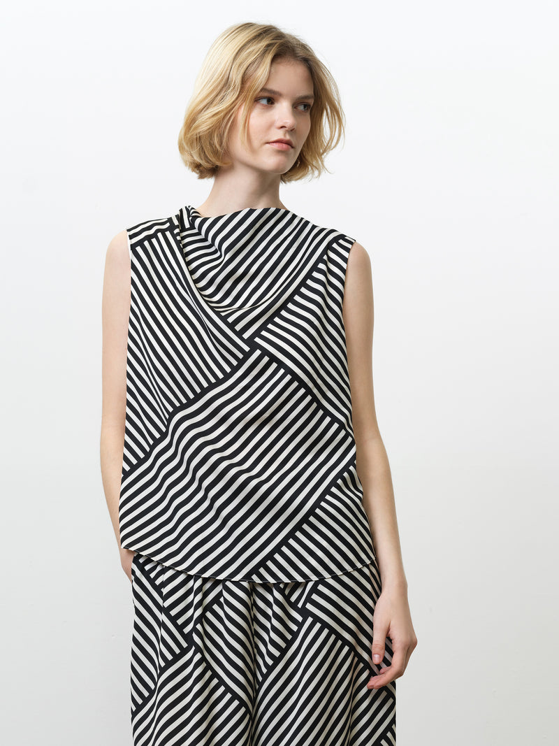 Woman wearing a black and white asymmetric striped sleeveless top with a cowl neckline and matching trousers