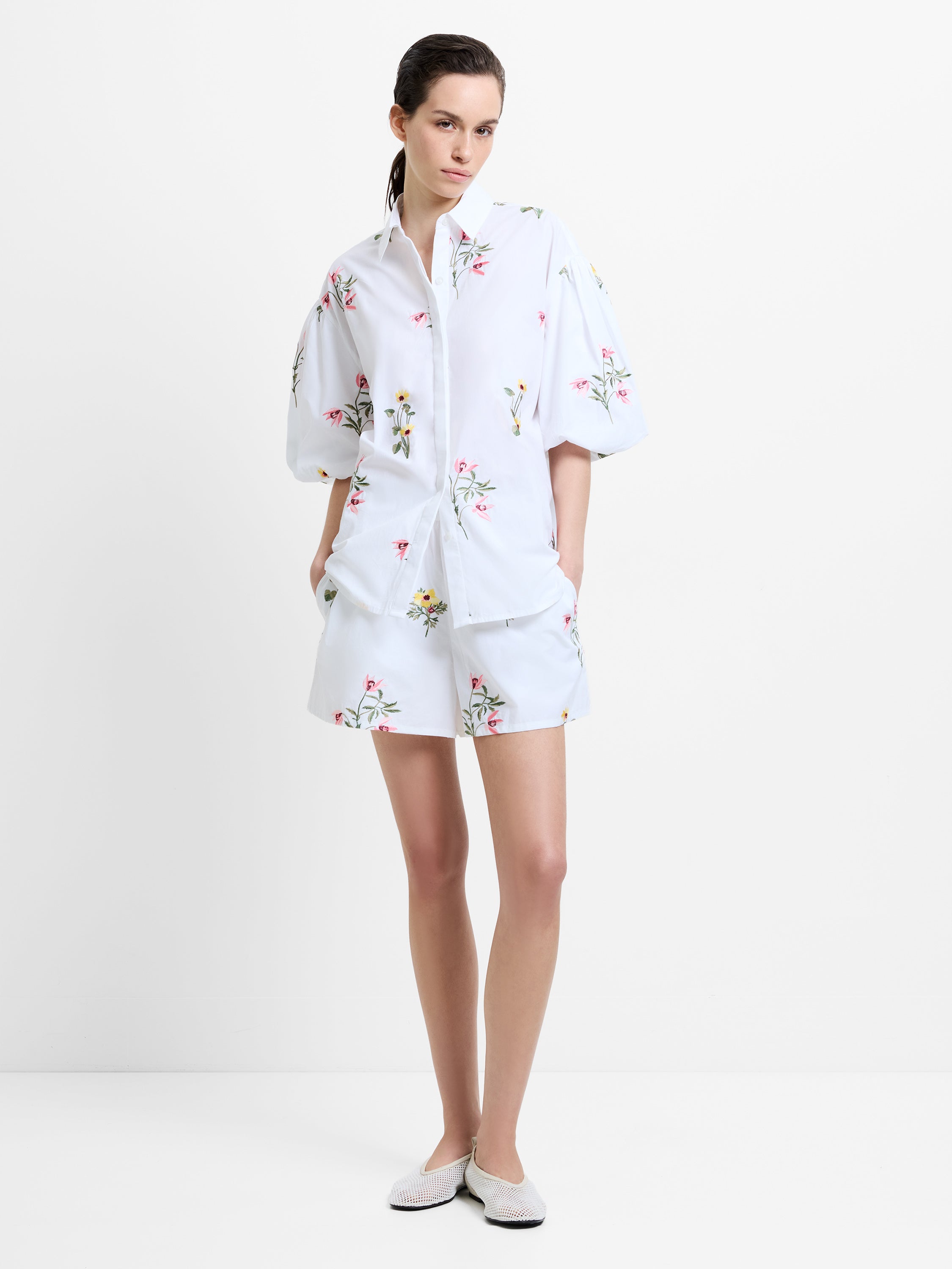 Woman wearing a floral embroidered white shirt and shorts matching set