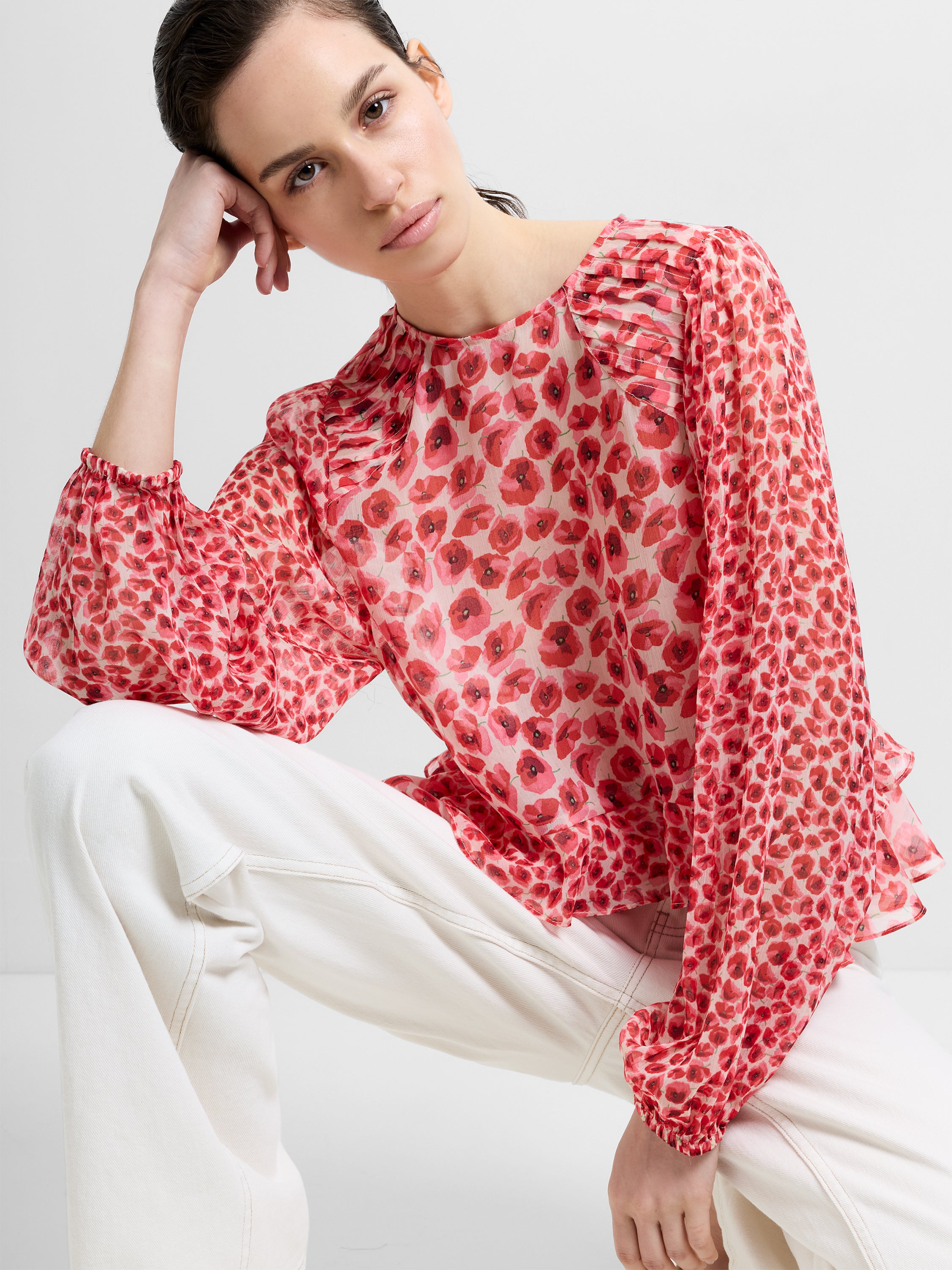Woman wearing a red poppy printed semi-sheer blouse, with long crinkle sleeves and a round neckline