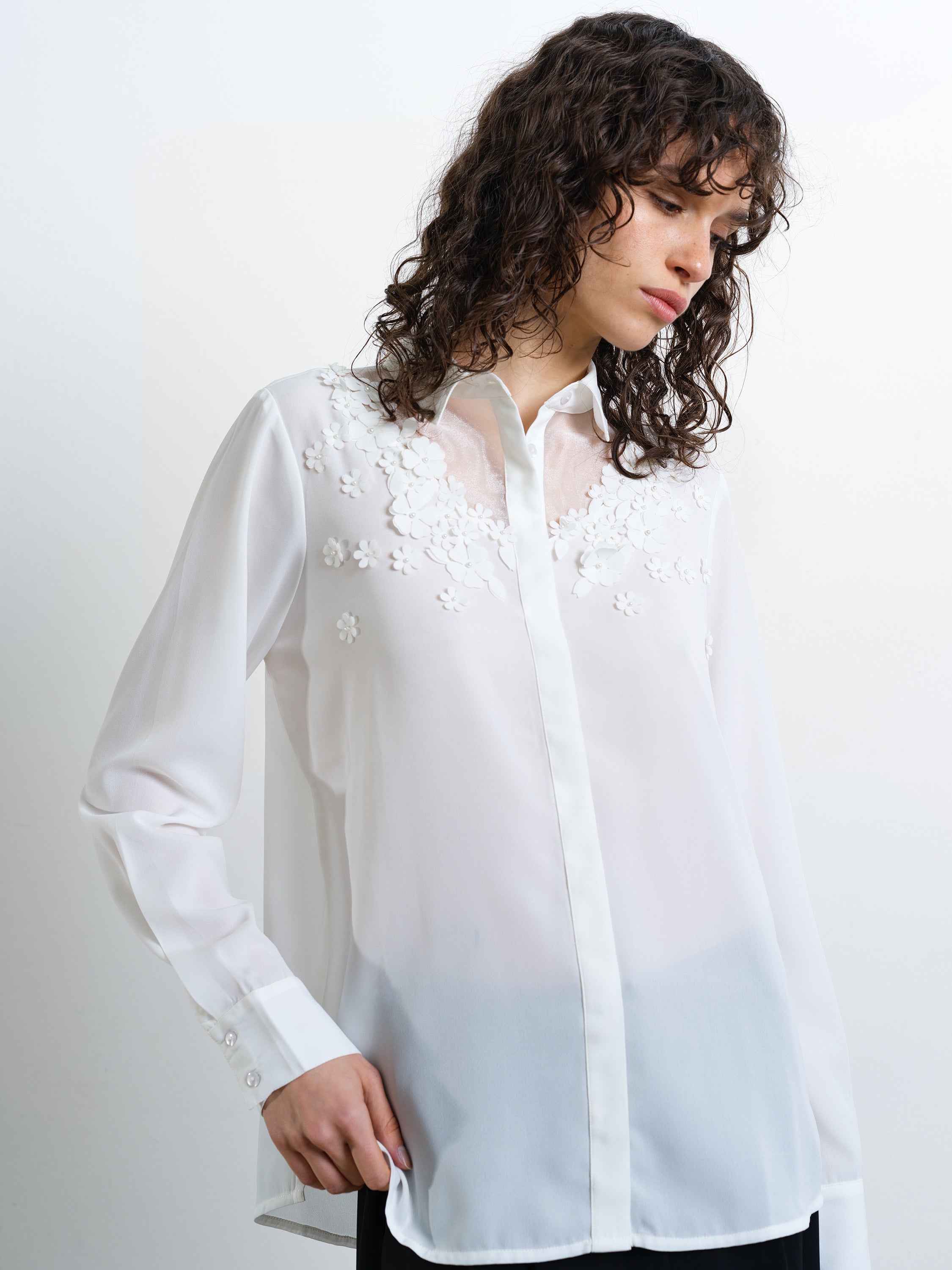 Woman wearing a semi-sheer white long sleeve shirt with concealed button down fastening and floral and pearl embellishment detailing