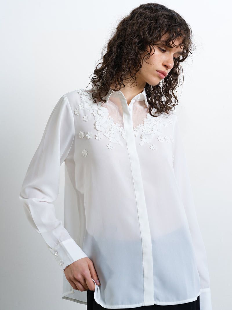 Woman wearing a semi-sheer white long sleeve shirt with concealed button down fastening and floral and pearl embellishment detailing
