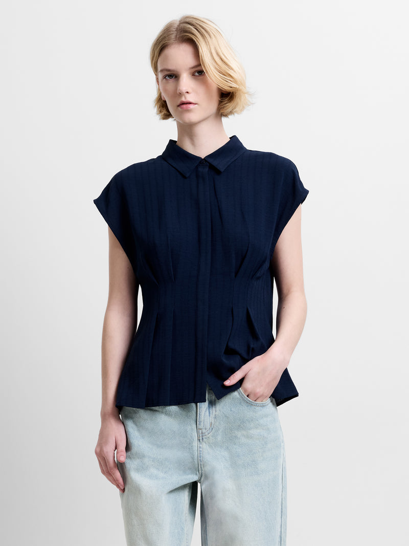 Woman wearing a navy short sleeve collared shirt, featuring a peplum shape and pleated waist detailing with concealed button down fastening