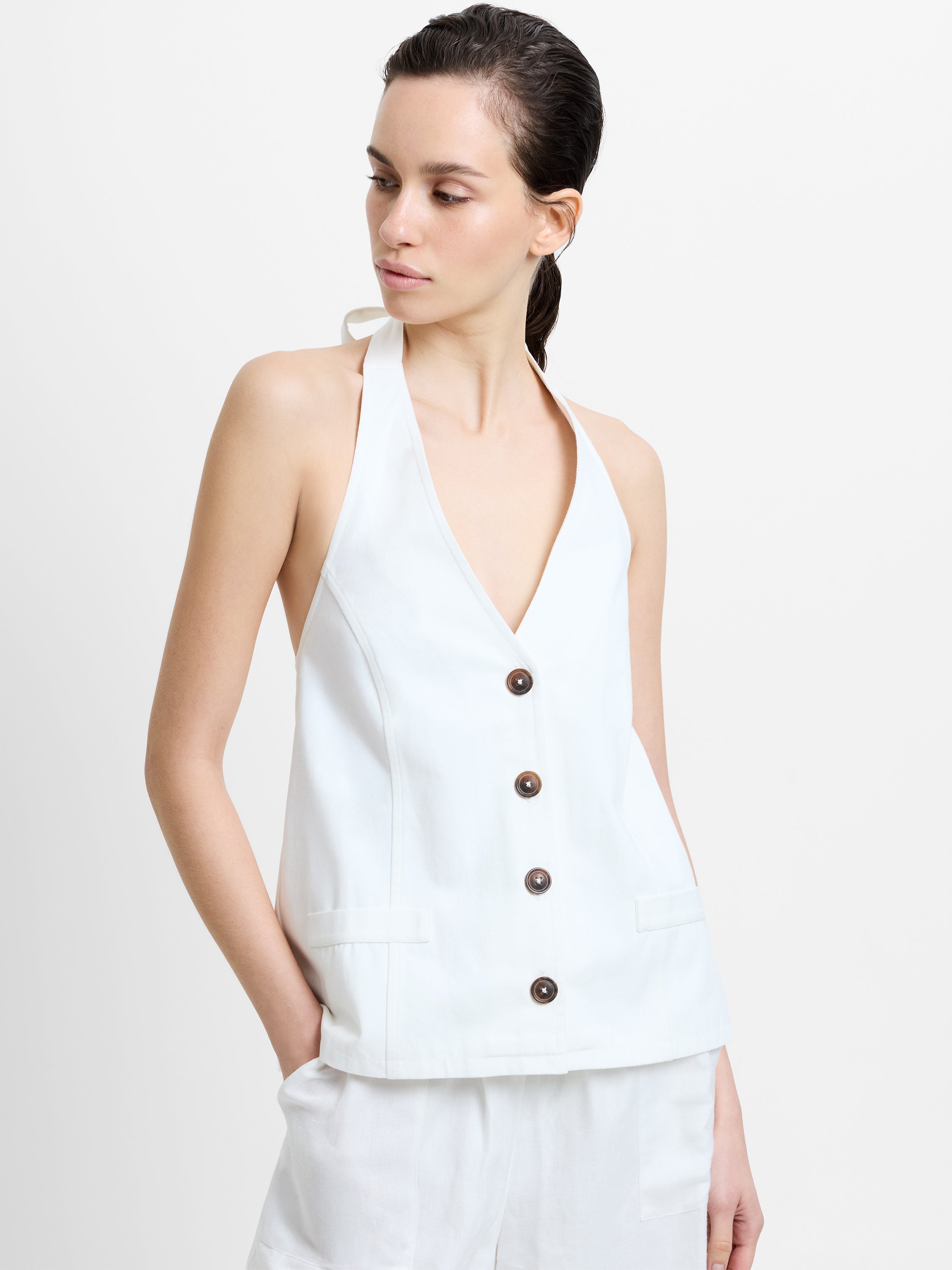 Woman wearing a white halterneck top with a deep V neckline and button down fastening