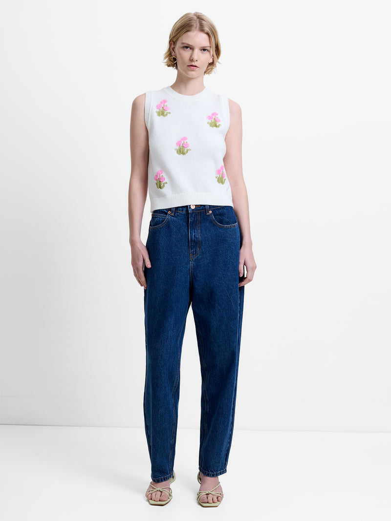 Woman wearing a cream knitted vest top with floral embellishments and dark blue mom barrel leg jeans
