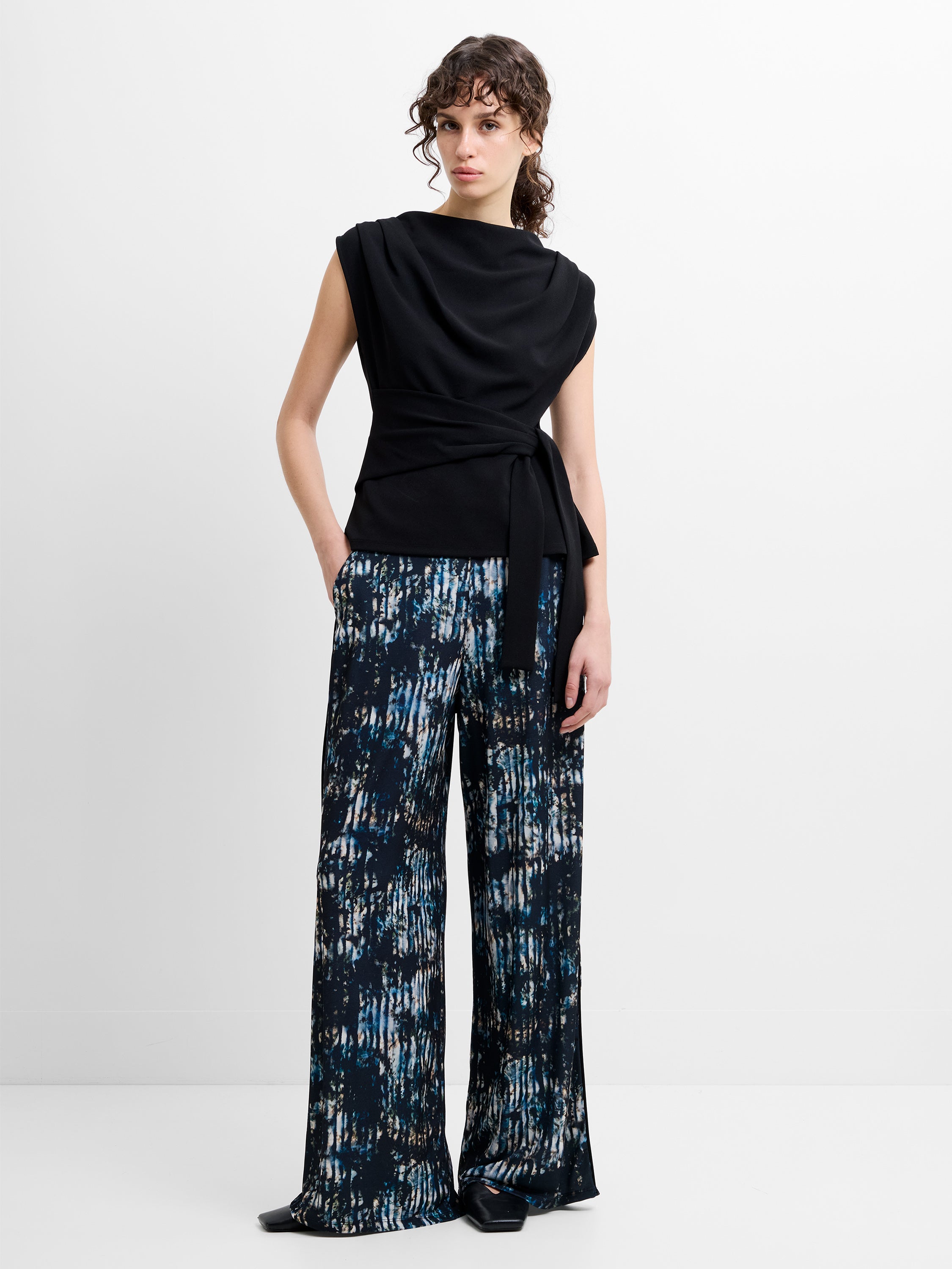 Woman wearing a black sleeveless top and wide leg blue abstract printed trousers