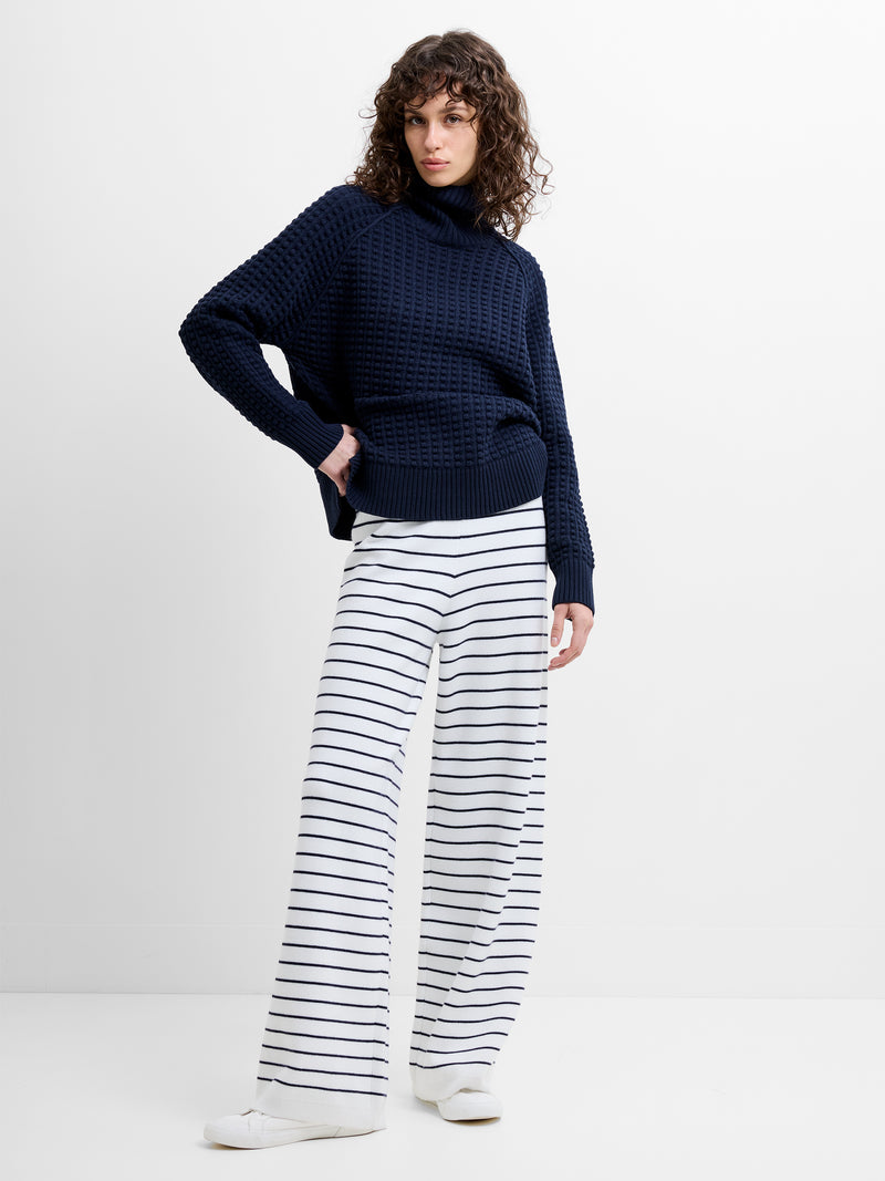 Woman wearing a navy jumper with striped wide leg white and blue trousers