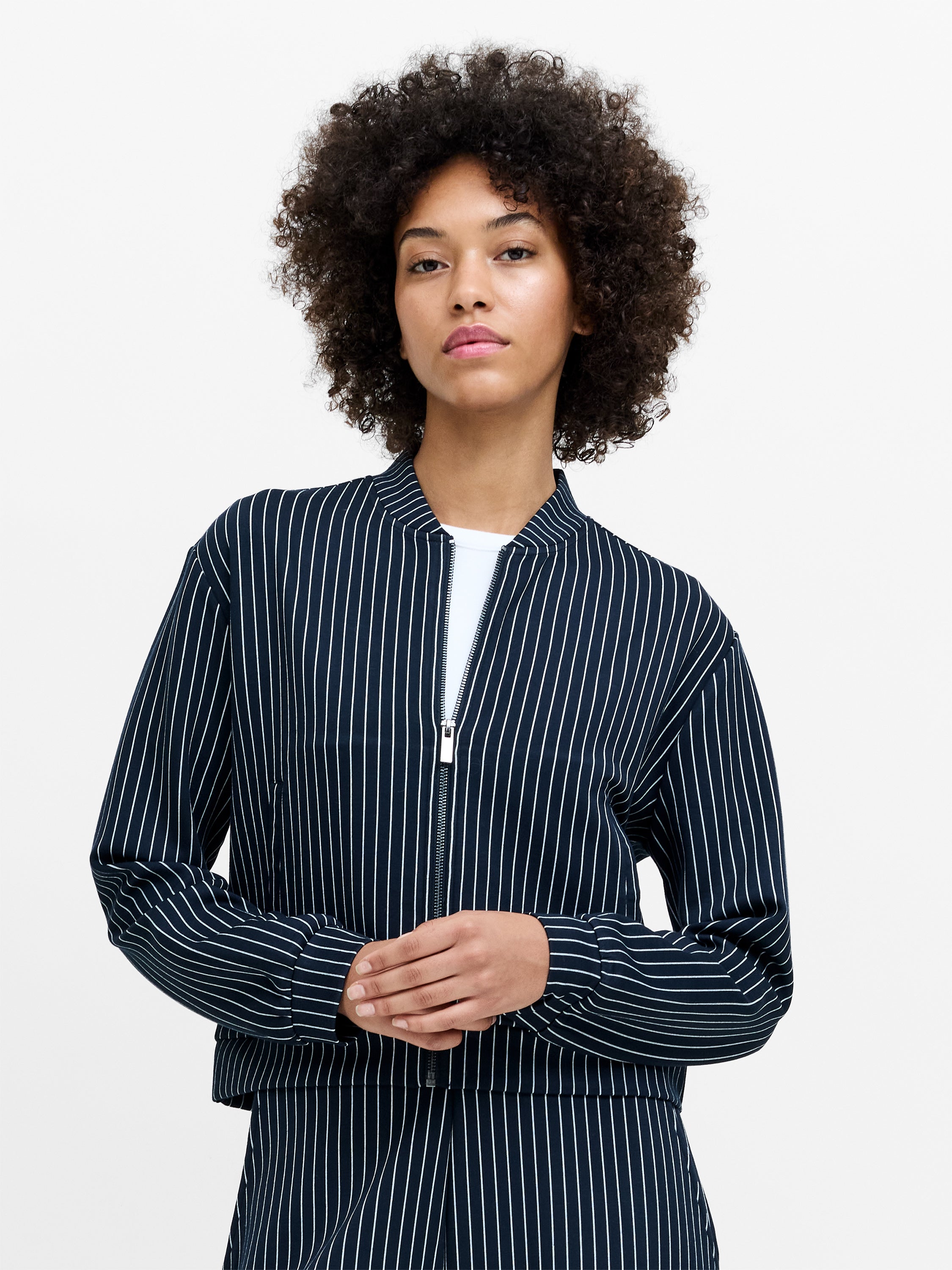 A woman wearing a pinstripe navy blue bomber jacket with a metal zip fastening, four pockets and long sleeves with fitted cuffs.