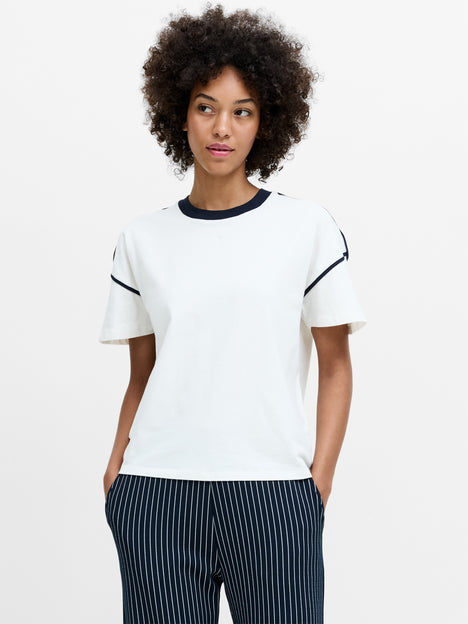 A woman wearing a relaxed fit white sort sleeved T-shirt with a black crew neck and a black contrast side trim. 