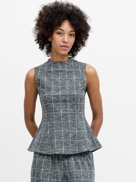 A woman wearing a sleeveless grey checked peplum top, with a high neckline, and a back zip.