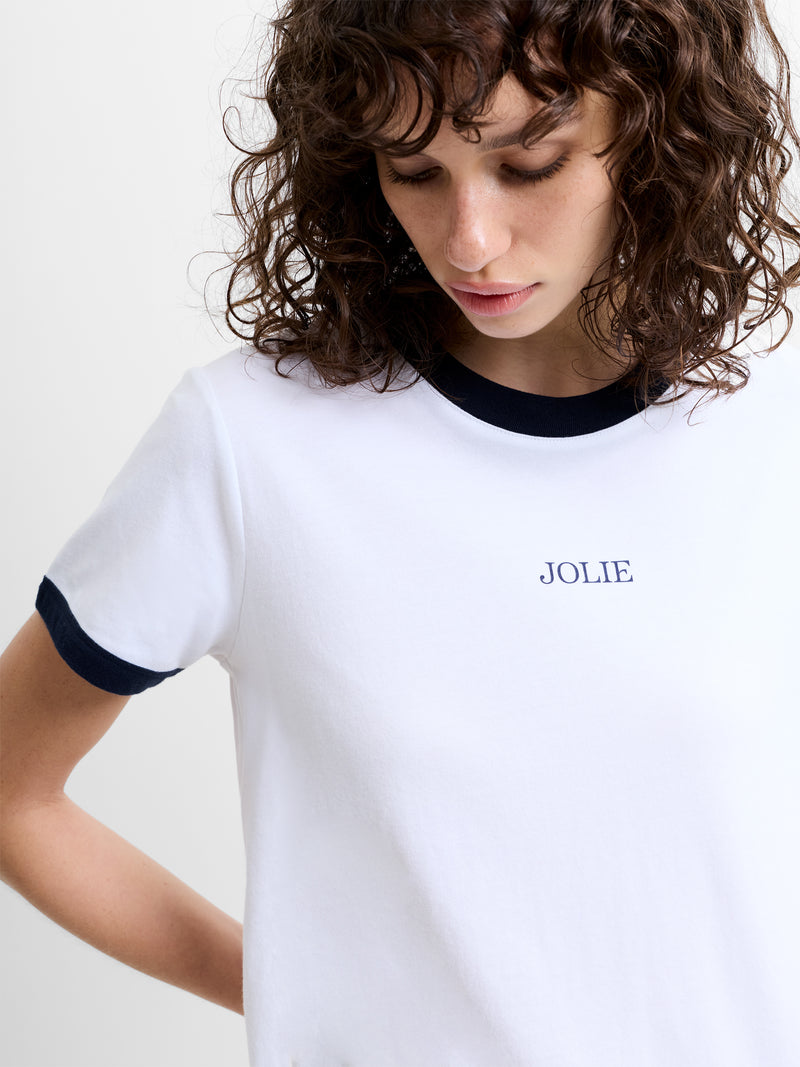 Person wearing a white short sleeve T-shirt with 'JOLIE' graphic