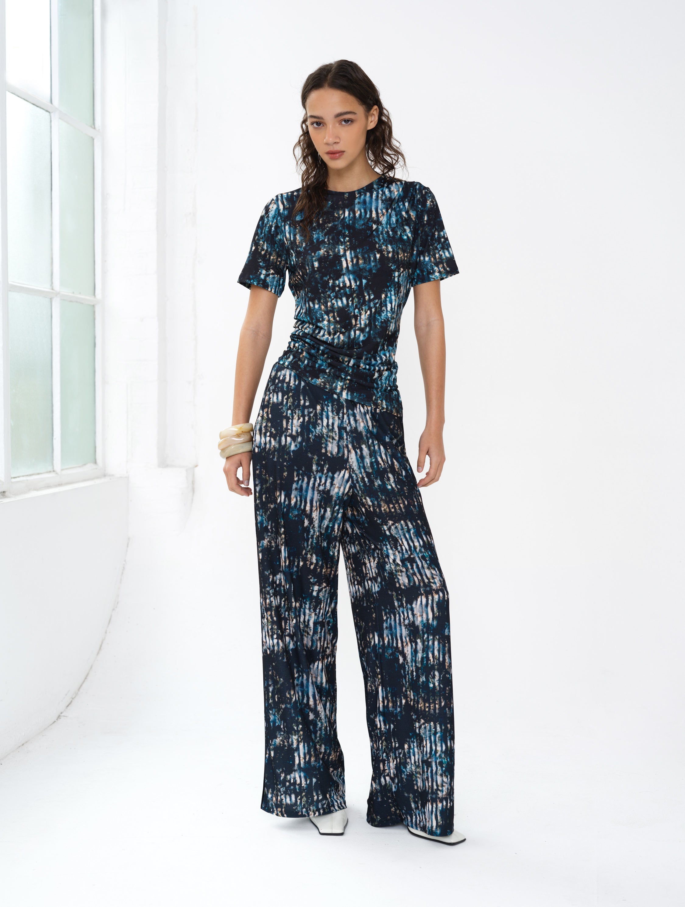 Woman wearing an abstract printed co-ord. A short sleeve draped top and wide leg trousers.