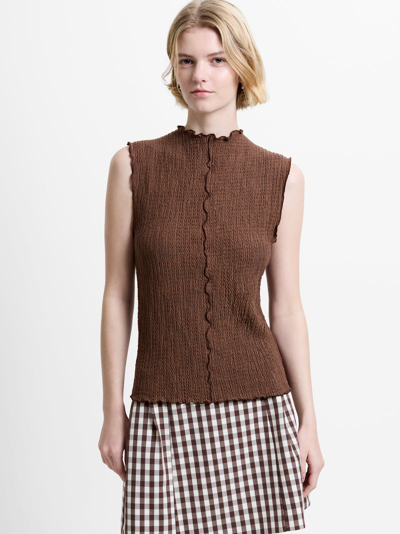 Woman wearing a brown textured sleeveless top, with lettuce trim detailing