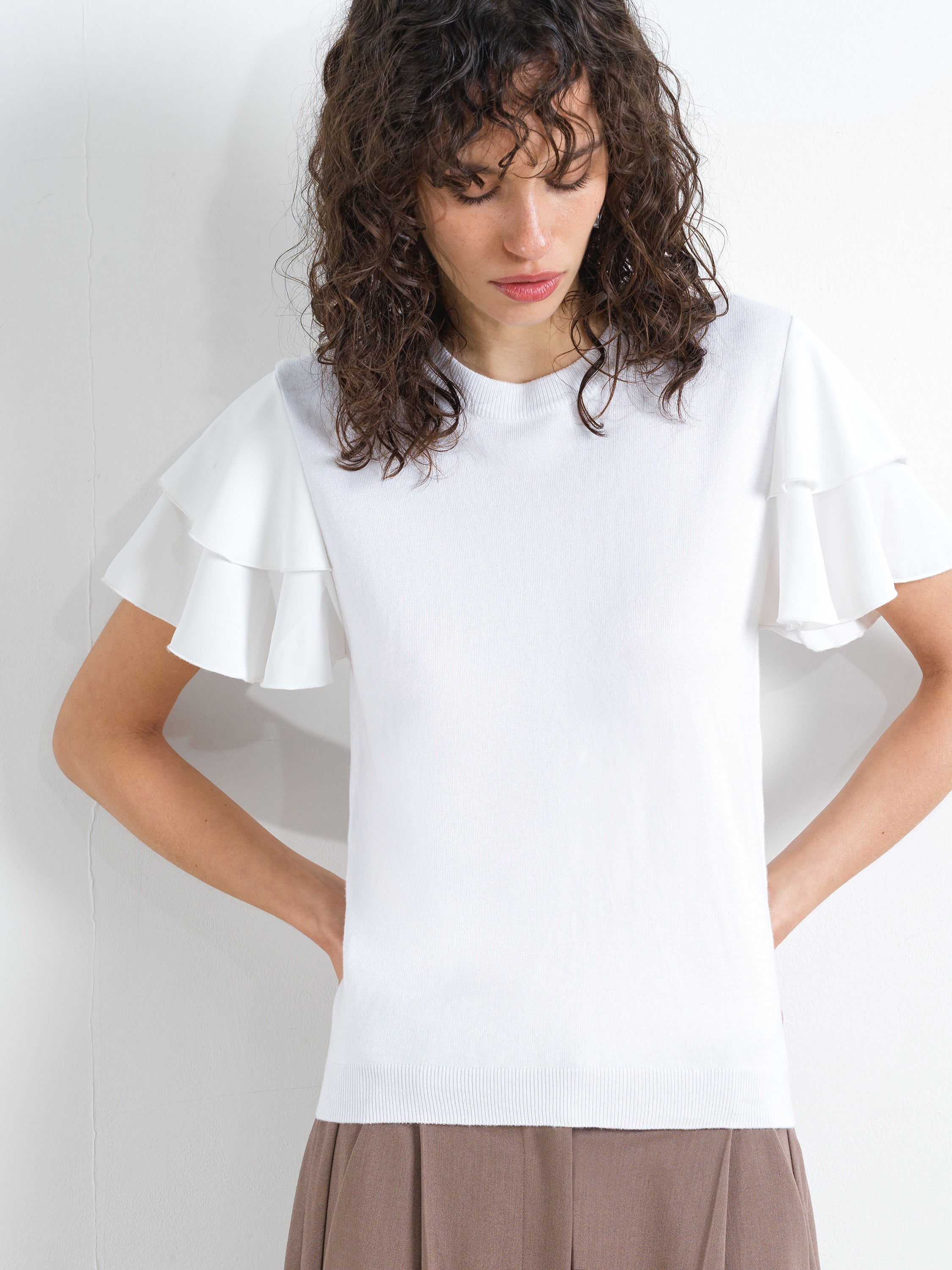 Woman wearing a white slim fit knitted top with a ribbed crew neckline and short ruffled sleeves