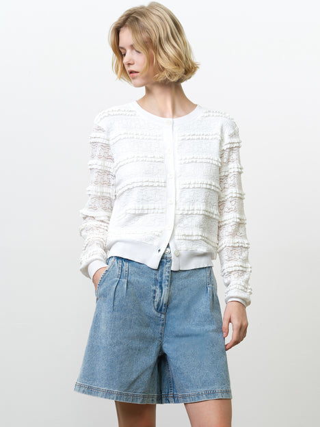 Woman wearing a long sleeve ruffled white cardigan with a lace overlay and semi-sheer sleeves