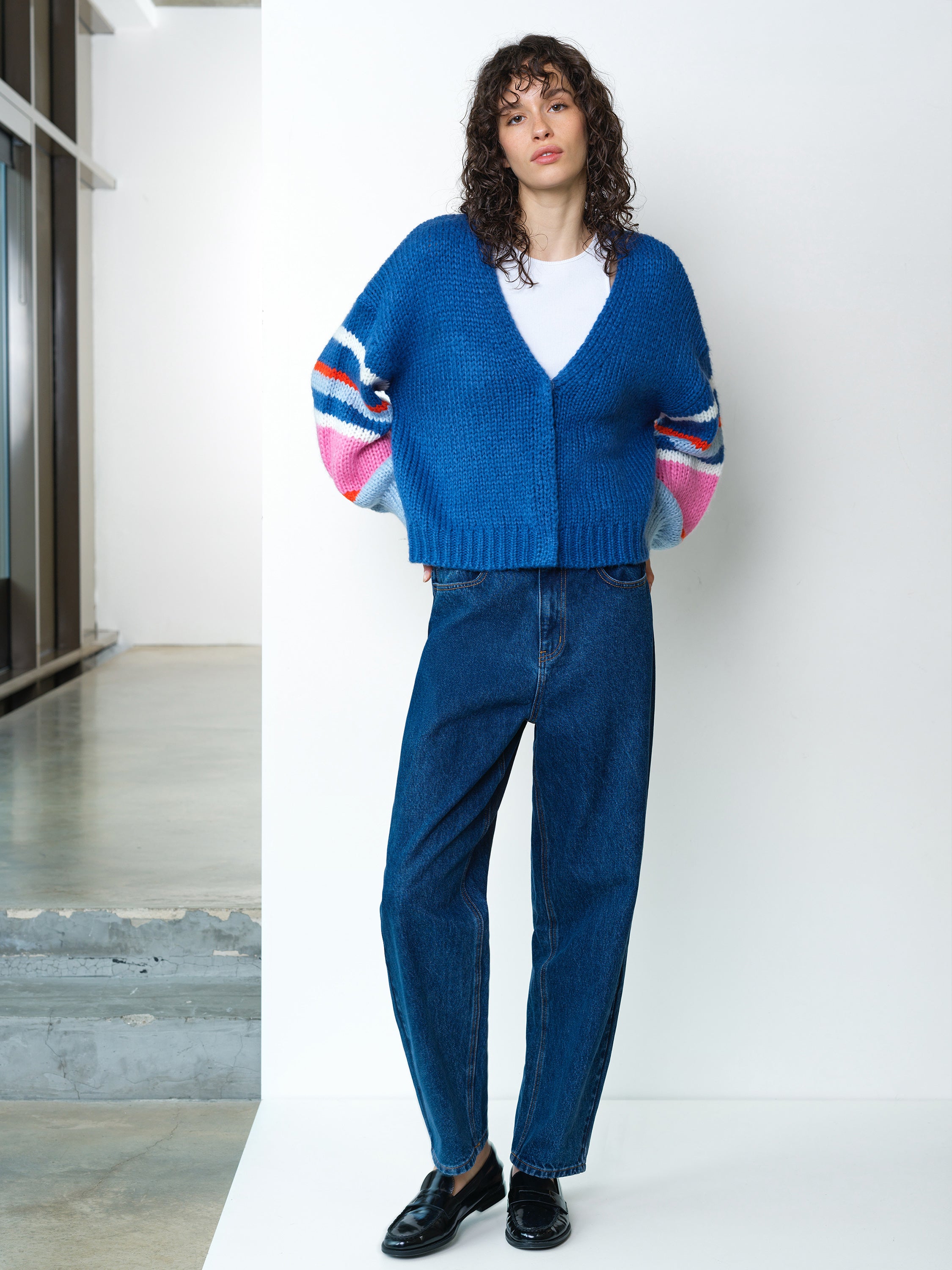 Woman wearing a long sleeve, V-neck dark blue cardigan, with multicoloured striped sleeves and concealed popper down fastening