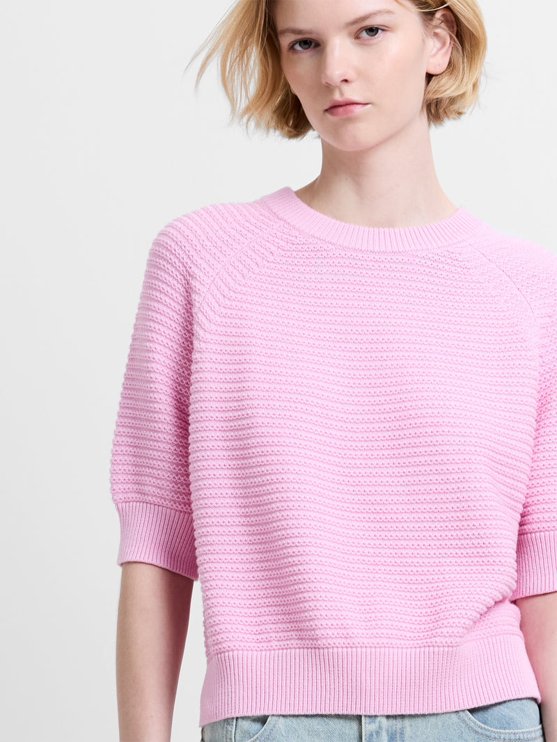 Woman wearing a baby pink, short sleeve jumper with a ribbed crew neckline and ribbed cuffs