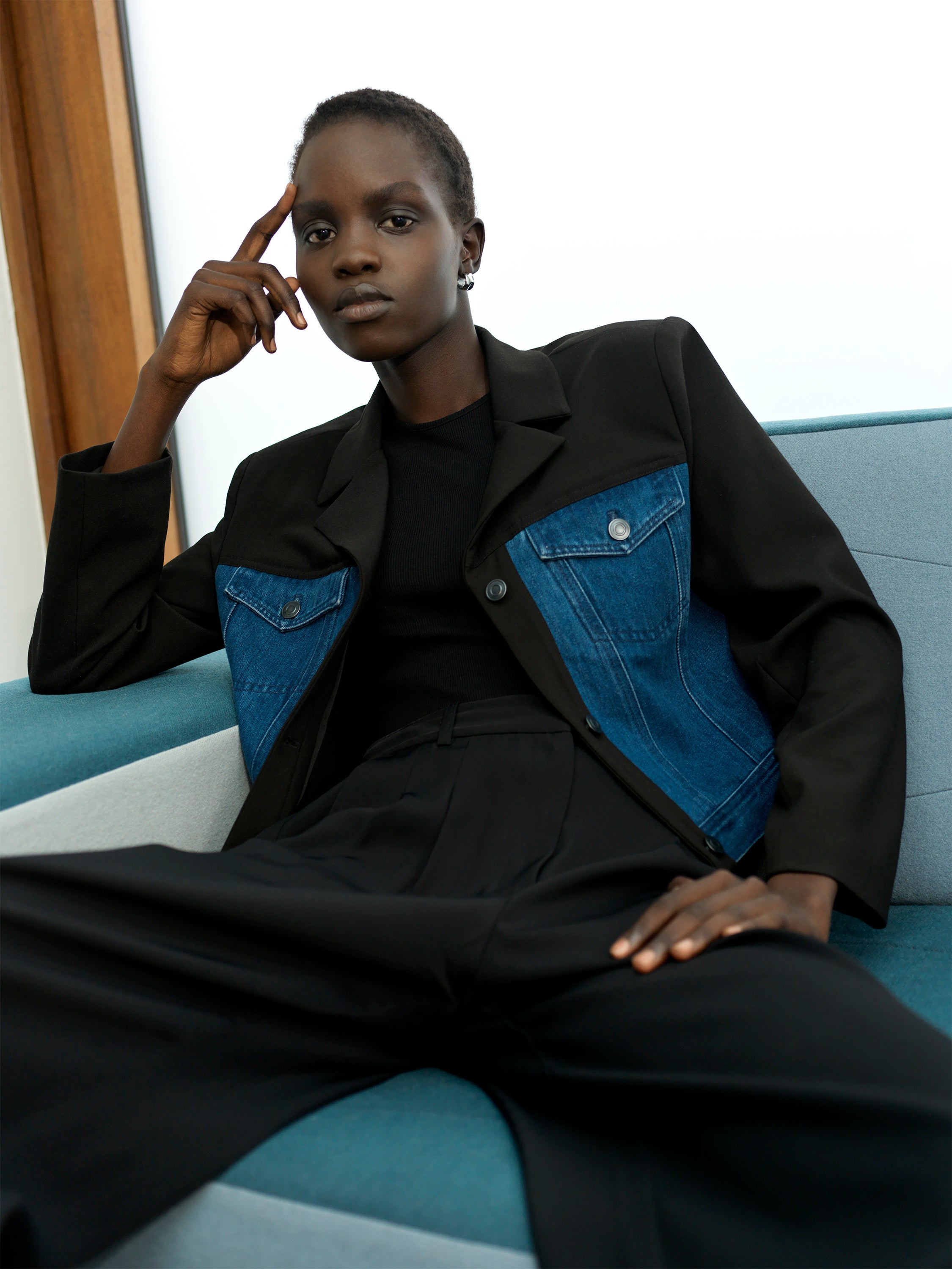 Woman wearing a tailored, mixed fabric jacket with a denim cropped body, black long sleeves and a lapel collar