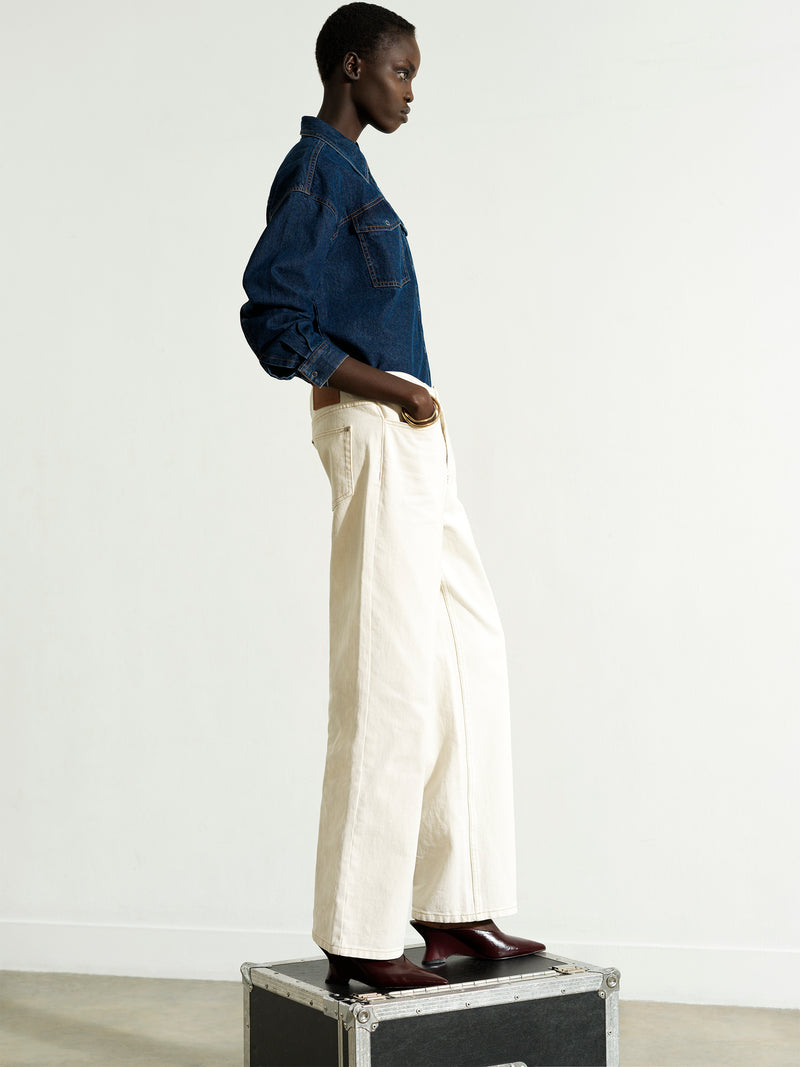 Woman wearing a dark blue denim shirt with high waisted, straight leg, clean waist jeans in ecru cream